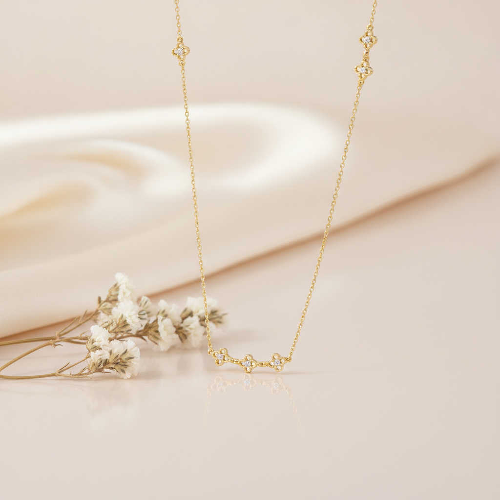 gold clover station necklace styled with dried baby's breath on a cream background