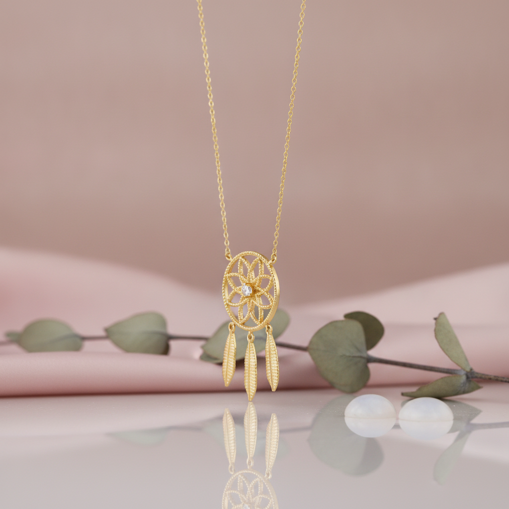 gold dreamcatcher pendant necklace with feather charms styled with eucalyptus and pearls on a pink background