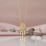gold dreamcatcher pendant necklace with feather charms styled with eucalyptus and pearls on a pink background