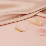 gold spike bar necklace styled with a dried rose and eucalyptus on a blush background