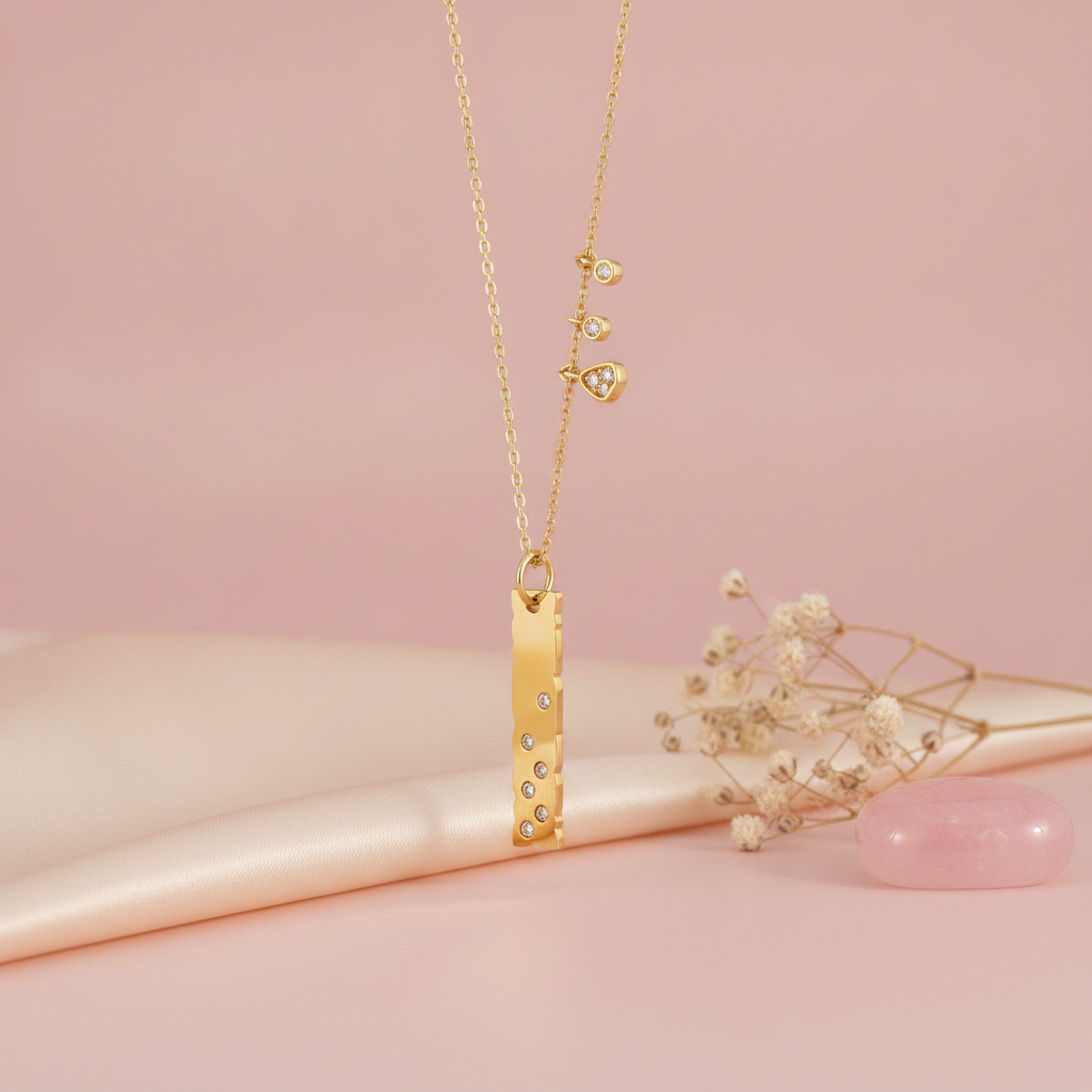 gold bar pendant necklace with dangling charms styled with dried flowers on a blush background