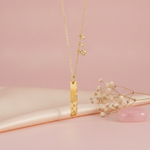 gold bar pendant necklace with dangling charms styled with dried flowers on a blush background