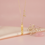 gold bar pendant necklace with dangling charms styled with dried flowers on a blush background