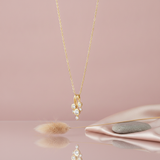 gold cascade drop necklace with clustered stones styled with pebbles on a cream background
