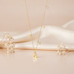 gold square charm necklace styled with dried baby's breath on a blush background