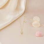 gold crescent moon and star pendant necklace styled with dried leaves and a pink stone on a cream background