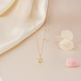 gold crescent moon and star pendant necklace styled with dried leaves and a pink stone on a cream background