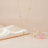 gold teardrop pendant necklace with charm stations styled with dried baby's breath and a pink stone on a blush background