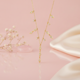 gold Y-necklace with a geometric drop styled with dried flowers and a pink stone on a blush background