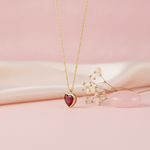 gold heart pendant necklace with a red stone styled with dried baby's breath and a pink stone on a blush background