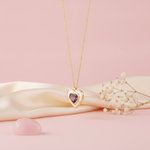 gold heart pendant necklace with a purple stone and white enamel styled with dried baby's breath on a blush background
