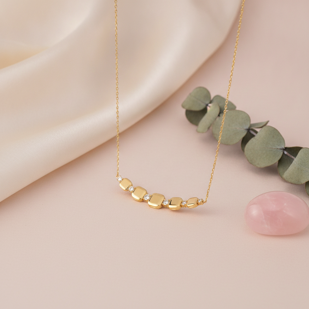 gold cushion station necklace styled with eucalyptus and a pink stone on a cream background