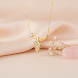 gold arrowhead pendant necklace styled with dried flowers on a blush background