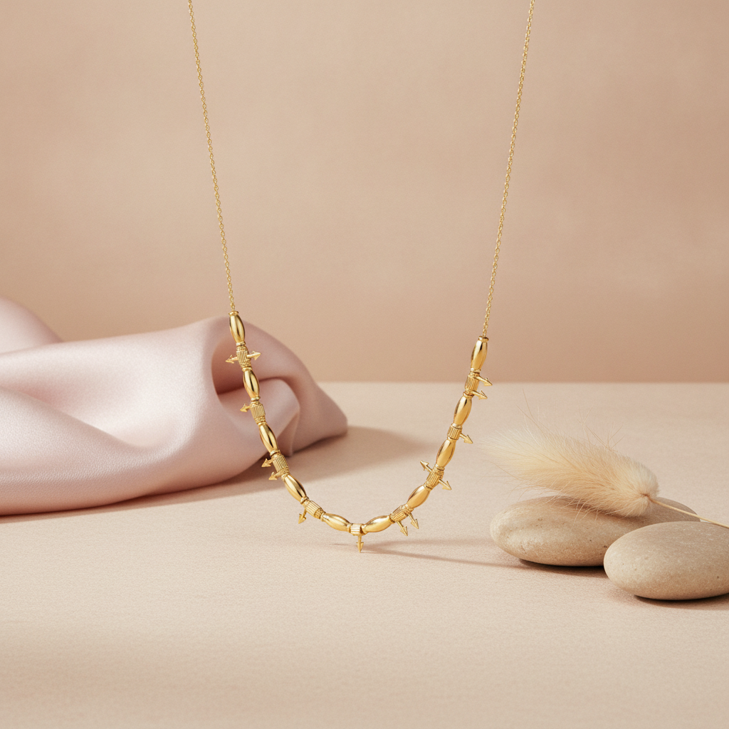 gold beaded necklace with arrow motifs styled with a feather and pebbles on a blush background