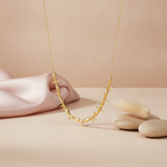 gold beaded necklace with arrow motifs styled with a feather and pebbles on a blush background