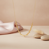 gold beaded necklace with arrow motifs styled with a feather and pebbles on a blush background