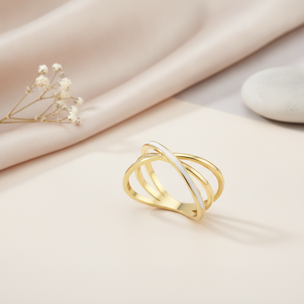 gold crossover ring with white enamel inlay styled with dried flowers on a blush background