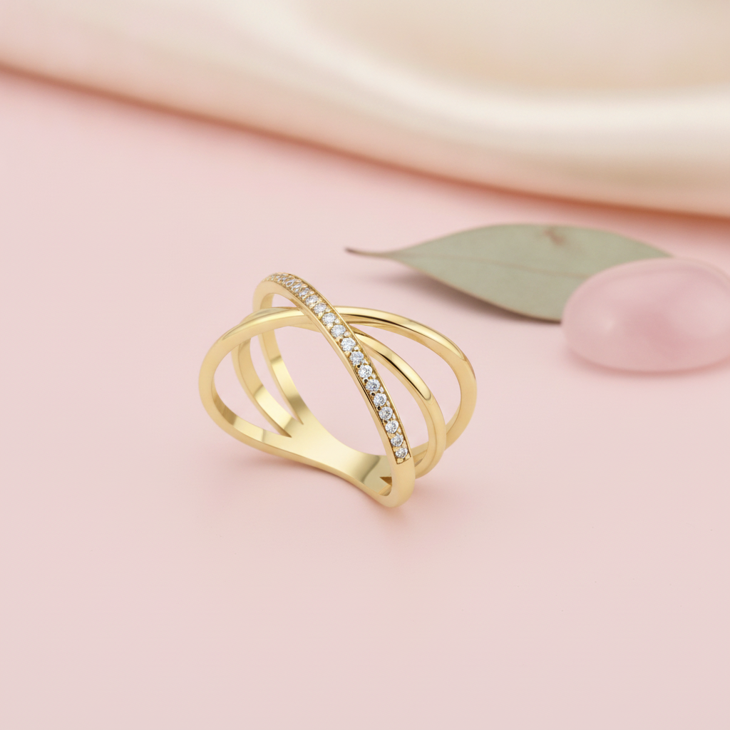 gold crossover ring with pave stones styled with a leaf and a pink stone on a blush background