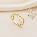 gold crossover ring with white enamel and a baguette stone styled with dried flowers on a cream background