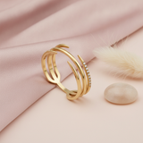 gold claw wrap ring with pave stones styled with a feather and a pebble on a blush background