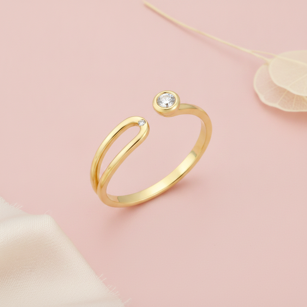 open bypass gold ring with a bezel-set round stone and a small accent stone, styled with a dried leaf on a pink background