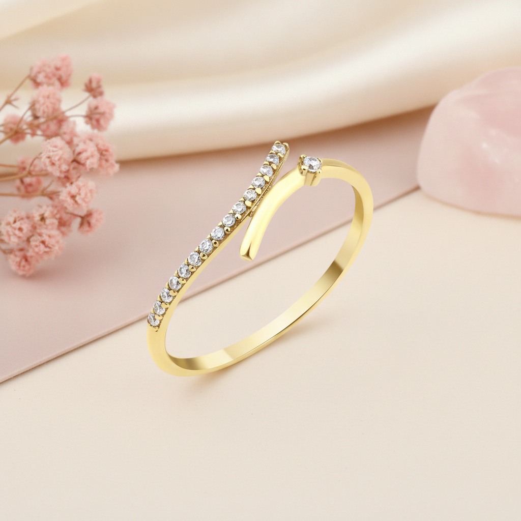 open wrap gold ring with a diagonal pave bar and a single round stone, styled with pink dried flowers on a blush background