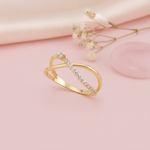 open crossover gold ring with a paved arch and a single solitaire stone, styled with dried flowers on a blush background