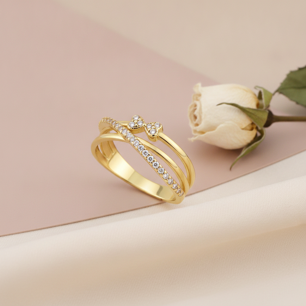 crossover gold ring with a pave strand and twin heart motifs set with clear stones, styled with a white rose on a blush background