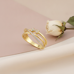 crossover gold ring with a pave strand and twin heart motifs set with clear stones, styled with a white rose on a blush background