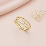 multi-strand gold ring with beaded, pave, and cone-tipped bands, styled with a dried flower on a blush background