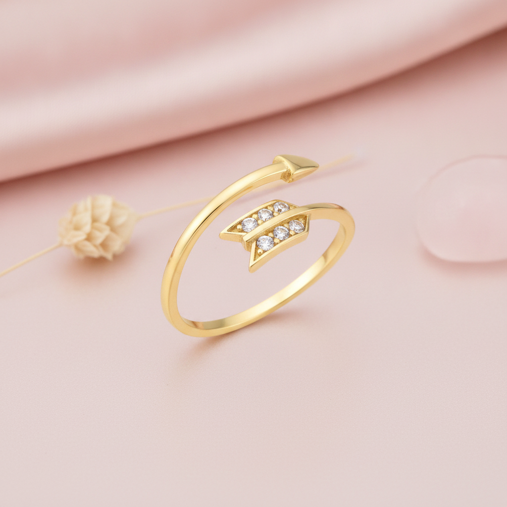arrow-shaped open gold ring with a pave chevron fletching, styled with a dried flower on a pink background