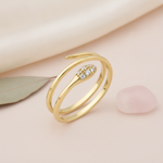 coiled gold serpentine ring with a stone-set tapered head, styled with a dried sage leaf on a cream background