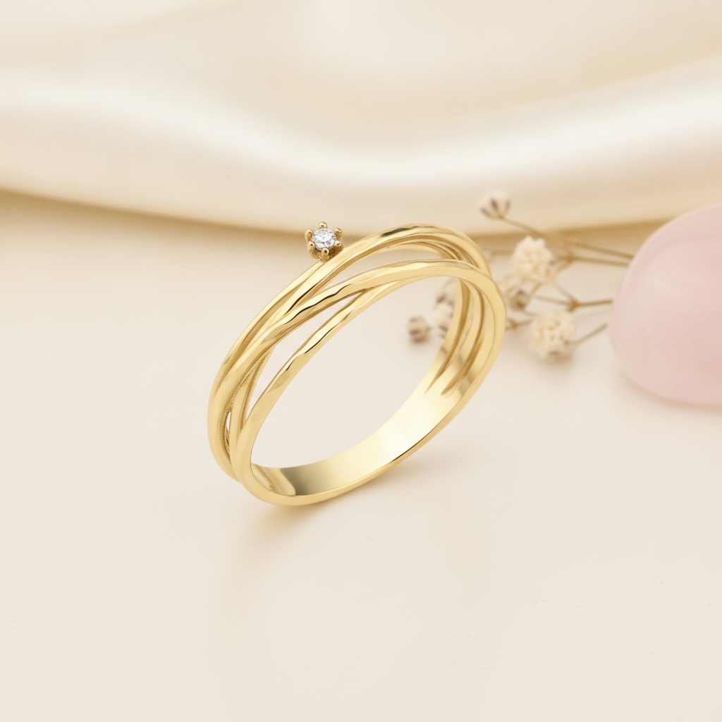 gold ring with three organic woven strands and a single prong-set stone, styled with a dried leaf on a cream background