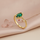 gold ring with an oval green stone and White CZ accents on a beaded band, styled with a dried pink leaf on a blush background