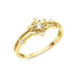 yellow gold ring with a sunburst motif, central clear stone, and beaded band on white background