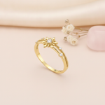 gold ring with a sunburst motif, central clear stone, and beaded band, styled with baby's breath on a blush background