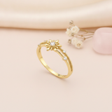 gold ring with a sunburst motif, central clear stone, and beaded band, styled with baby's breath on a blush background