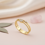 dual-band gold ring with a pave heart motif and accent stones, styled with dried flowers on a blush background