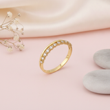 gold ring with a smooth band and a parallel arc of prong-set clear stones, styled with dried flowers on a blush background