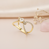 open bow-shaped gold ring with pave loops and a marquise-cut stone cluster, styled with dried flowers on a blush background