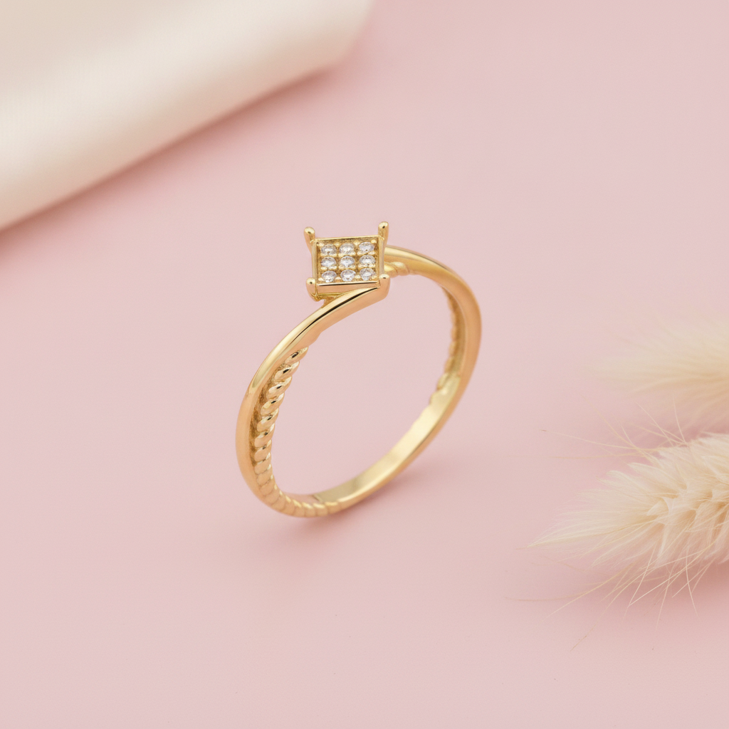 gold ring with a square pave crest and a twisted rope band, styled with a dried grass sprig on a blush background
