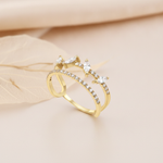 open double-band gold ring with pave stones and marquise-cut accents, styled with a dried leaf on a blush background