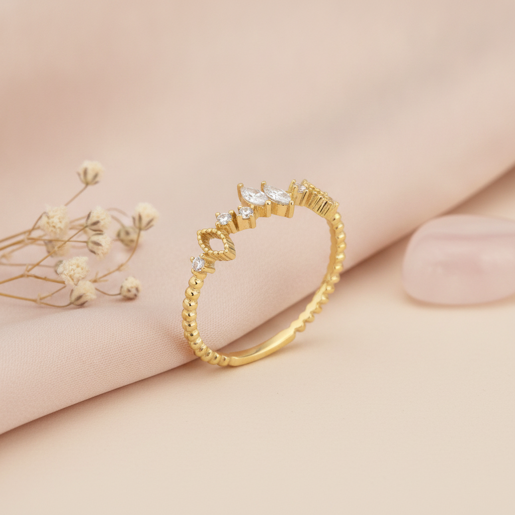 gold ring with marquise-cut and round stones on a textured geometric band, styled with dried flowers on a blush background