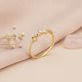 gold ring with marquise-cut and round stones on a textured geometric band, styled with dried flowers on a blush background
