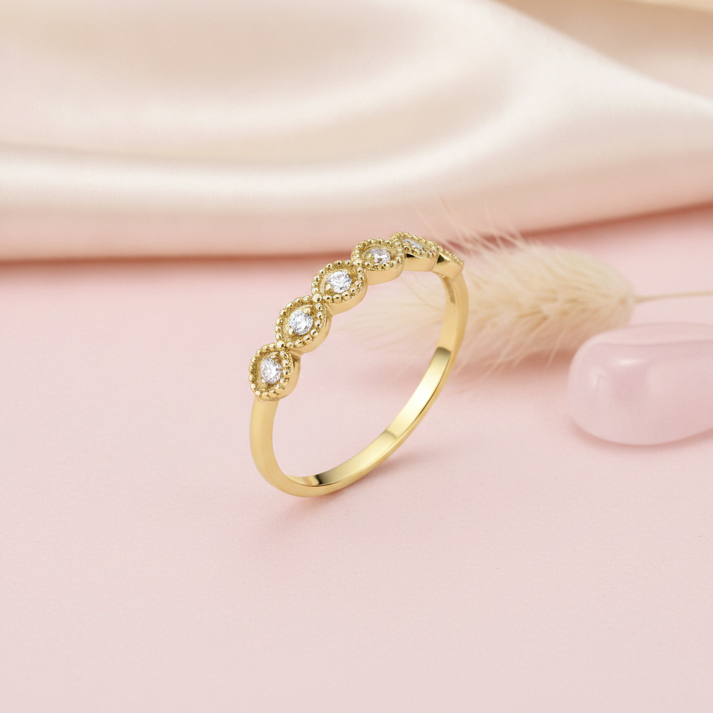 gold ring with six round stones in milgrain bezels, styled with a dried flower and a pebble on a blush background