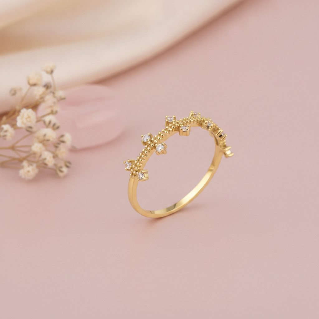 gold ring with staggered clear prong-set stones on a beaded band, styled with dried flowers on a blush background
