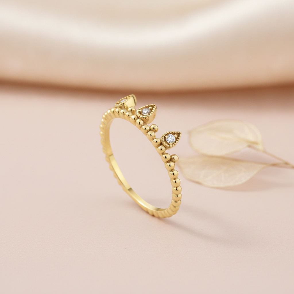 gold ring with three teardrop crown crests set with clear stones, styled with a dried leaf on a blush background