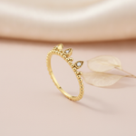 gold ring with three teardrop crown crests set with clear stones, styled with a dried leaf on a blush background