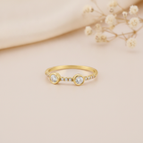 gold ring with round bezel-set clear stones and a pave accent path, on blush fabric with dried baby's breath