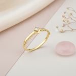 gold chevron ring with beaded edging and a single square clear stone, on cream fabric with dried flowers and a pink stone